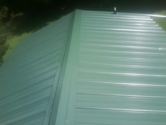 New green metal panels meeting at the ridge of a roof — Flat Roof Repair work by our crew in Riverside